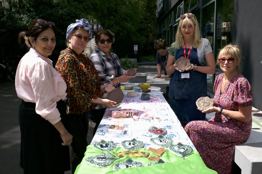 Members of the staff team pose around a table displaying a range of ceramics, being created to commemorate the Grenfell Tower fire.